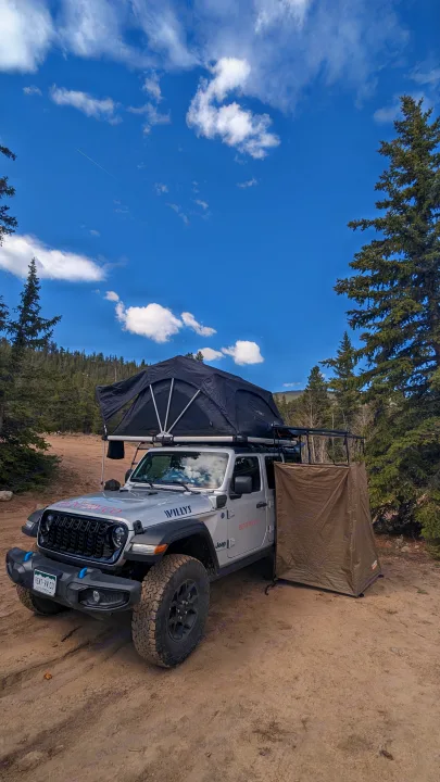 RV rental Jeep with rooftop tent & privacy shelter for off-road camping adventures under a blue sky.. Jeep Wrangler 2024