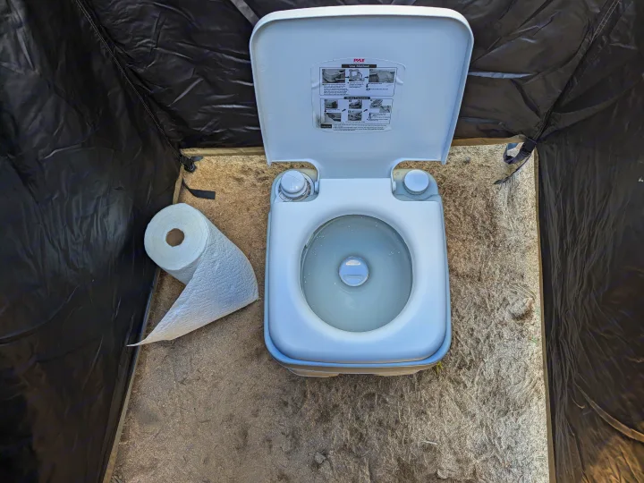 RV rental essential: Portable toilet inside a camping privacy tent, with toilet paper on sand.. Jeep Wrangler 2024