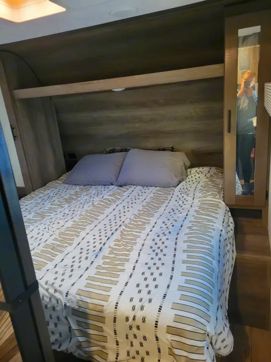 RV rental bedroom featuring a patterned bedspread, cozy pillows, and built-in storage with a mirrored closet.. KZ Confluence 2022