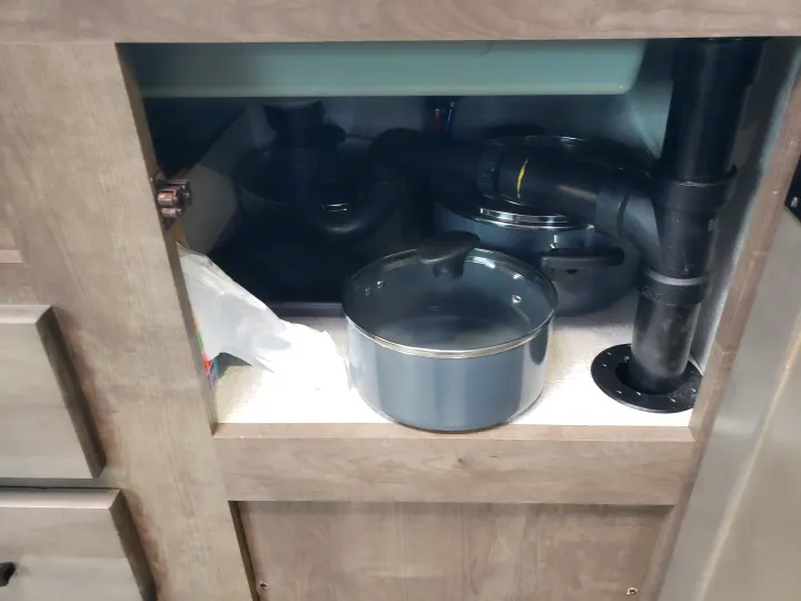 RV rental under-sink cabinet: view of drain pipes, pots, and a plastic bag in a compact kitchen space.. Venture Sonic SN211VDB 2022