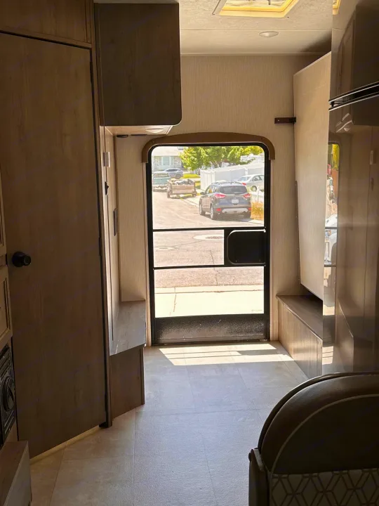 RV rental interior: View from inside towards the main entrance door, revealing wood cabinetry, tiled floor, and a sunny street.. Coachmen Freelander 2020