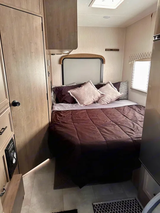 Cozy RV rental bedroom with a comfy bed, overhead cabinets, and a window for natural light. Ideal for travel trailer adventures.. Coachmen Freelander 2020