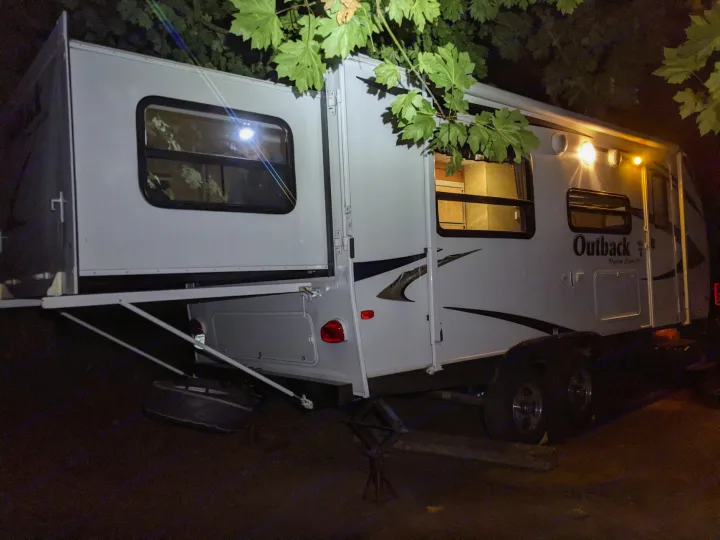 Illuminated Outback RV rental at night, its slide-out extended for more living space at the campsite.. Keystone RV Outback 2010