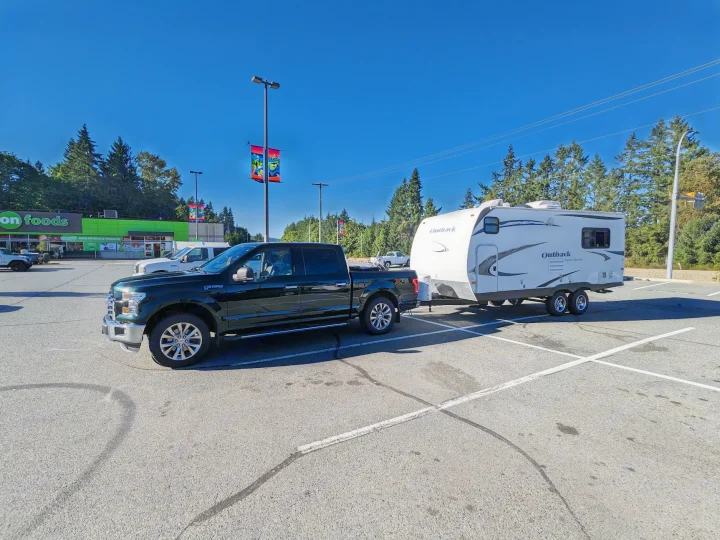 Dark pickup truck towing an Outback travel trailer (RV) in a sunny parking lot. Perfect for your RV rental adventure!. Keystone RV Outback 2010