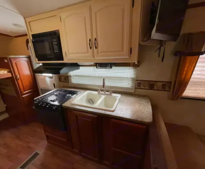 Interior of an rv rental: kitchen with microwave, stove, sink, plus dinette & bunk beds. Compact and functional design.. Keystone RV Outback 2010