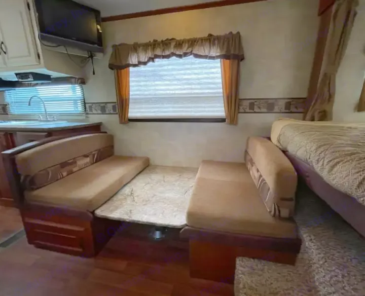 RV rental interior: dinette with table, kitchen sink, TV, and cozy bed. A compact, functional living space.. Keystone RV Outback 2010