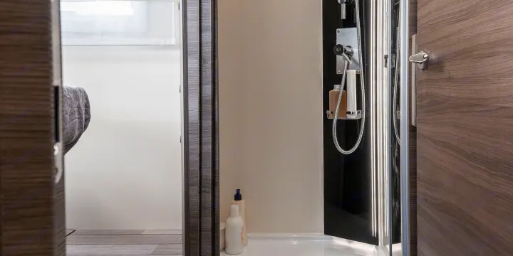 Modern RV rental interior with a compact shower and a peek into the bedroom area through an open door.. MCLOUIS YEARLING 89 2024
