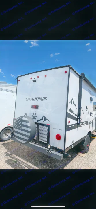 Back of a white Wolf Pup RV with mountain graphics, paw print, and a grey American flag tire cover, perfect for RV rental trips.. Forest River Cherokee Wolf Pup Black Label 2022
