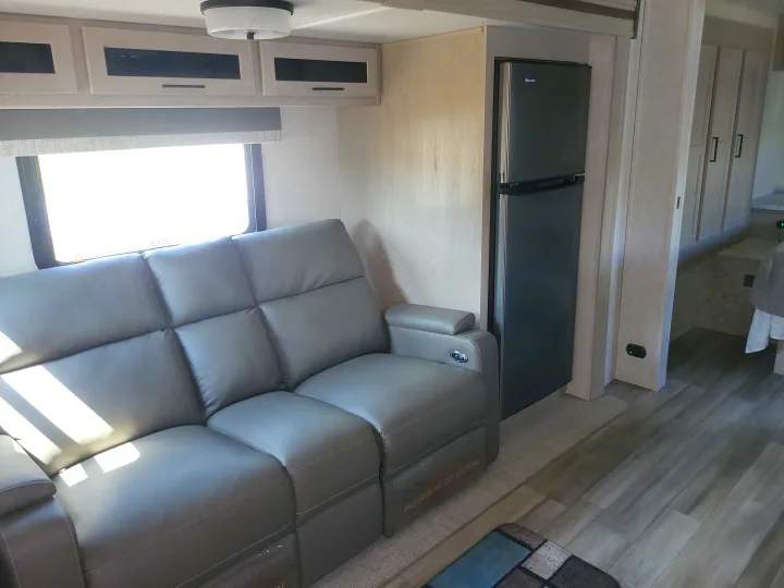 Cozy RV rental living space featuring a gray leather sofa, overhead cabinets, and a compact refrigerator.. Forest River Flagstaff Micro Lite 2023