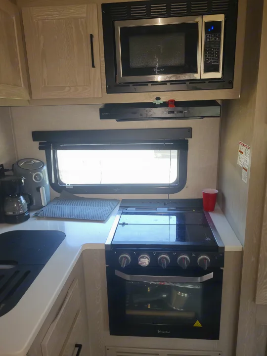 This rv rental kitchen features a microwave, stove, coffee maker, air fryer, and a bright window.. Forest River Flagstaff Micro Lite 2023