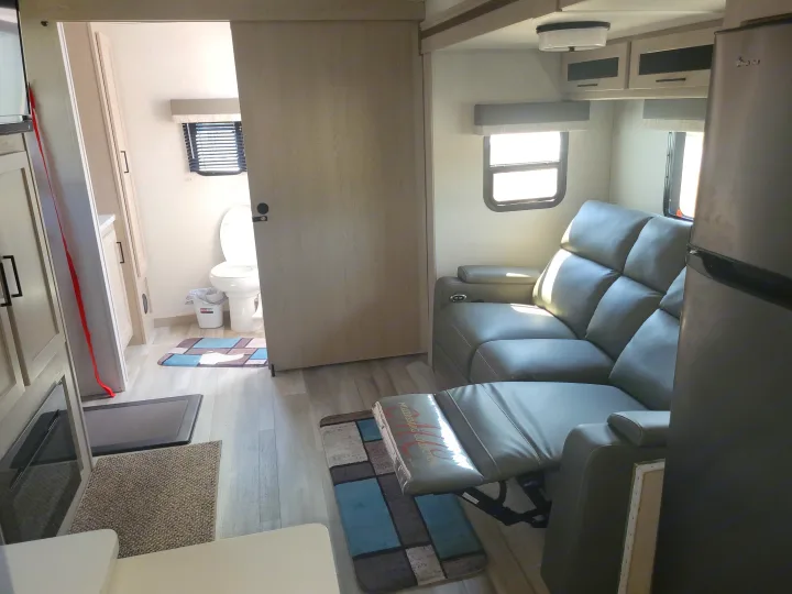 Inside an RV rental: A modern interior with a gray reclining sofa, large fridge, and open bathroom area with a toilet.. Forest River Flagstaff Micro Lite 2023