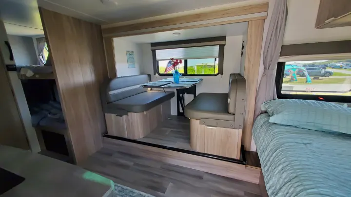 Cozy RV rental interior: a dinette, bunk beds on the left, and a comfortable main bed on the right.. Winnebago Minnie Winnie 2021