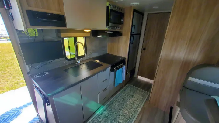 Well-equipped RV rental interior featuring a compact kitchen with sink, stove, microwave, and TV for comfortable travels.. Winnebago Minnie Winnie 2021