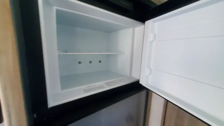 Empty, clean RV rental refrigerator with open door and shelf, ready for your travel essentials.. Winnebago Minnie Winnie 2021