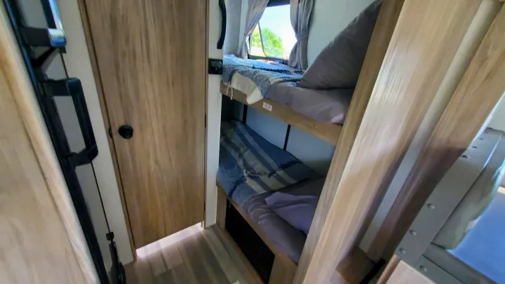 RV rental: Compact interior showing two bunk beds with bedding, a window view, and an adjacent wooden door.. Winnebago Minnie Winnie 2021