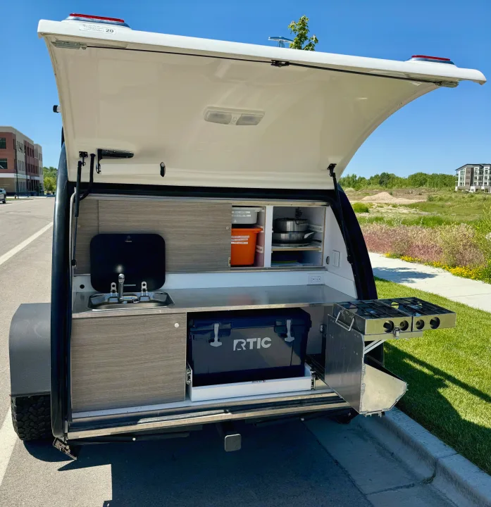 This RV rental teardrop trailer features a compact outdoor kitchen with a sink, two-burner stove, and RTIC cooler, ideal for camping.. Bean Trailer Bean Trailer Trailer 2019