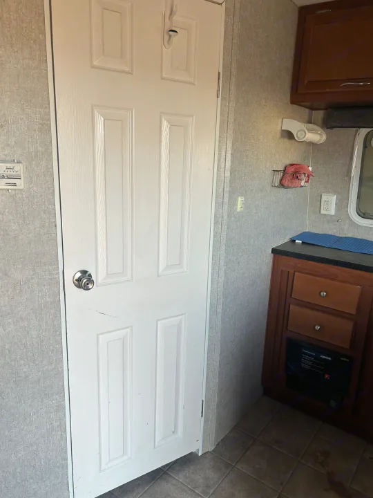 Inside an RV rental: features a white door, compact kitchen with brown cabinets & counter, plus a wall thermostat.. Eclipse Recreational Vehicles Stellar 2011
