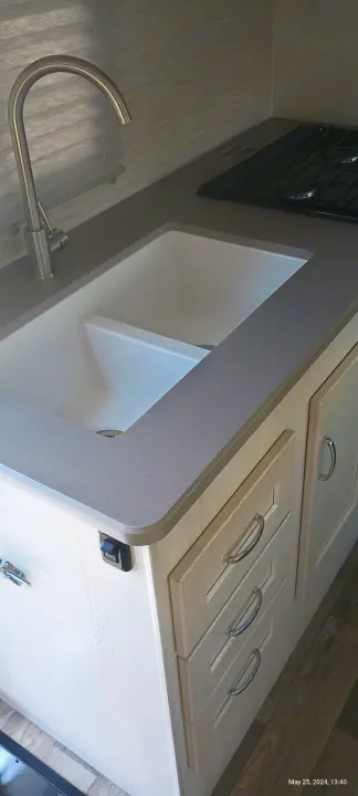 RV rental kitchen featuring a modern double sink with chrome faucet, stovetop, light wood cabinets, and grey countertop.. Winnebago Outlook 2021