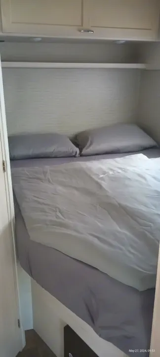 RV rental bed with grey pillows and duvet under overhead cabinets and shelf, a compact sleeping area.. Winnebago Outlook 2021