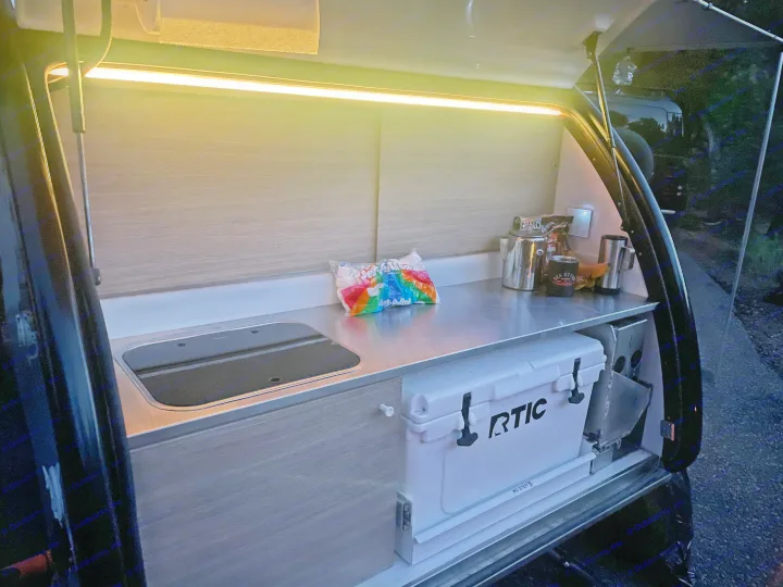 Bright RV rental kitchen/galley: stainless counter, built-in sink/stove, RTIC cooler, and marshmallows for camping.. Bean Trailer Bean Trailer Trailer 2019