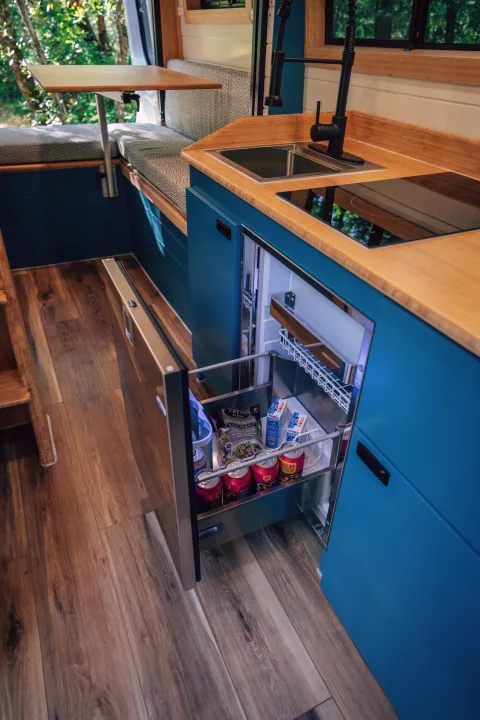 RV rental: functional kitchen with blue cabinets, bamboo counters, sink, cooktop, and a stocked fridge drawer. Dining area too.. Mercedes-Benz Sprinter 2024