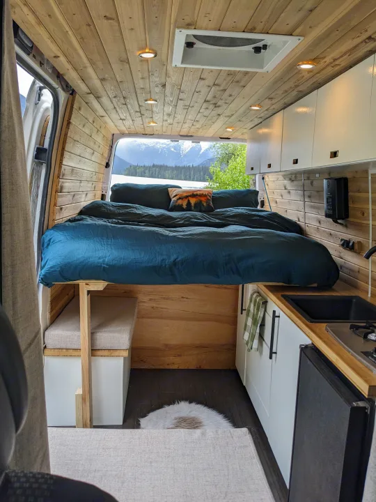 Cozy RV rental interior with a comfy bed, kitchenette, wood finish, and stunning mountain lake view. Perfect for adventures!. Dodge Sprinter Van 2007