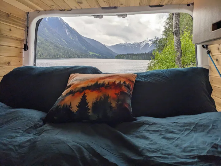 Inside a cozy RV rental: a comfortable bed with a scenic view of a vast mountain lake and snow-capped peaks.. Dodge Sprinter Van 2007