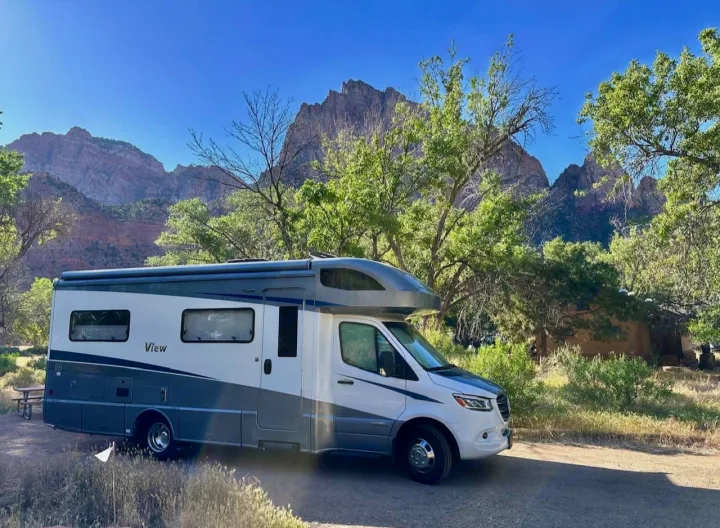 Experience the outdoors! An rv rental is parked in a scenic mountain landscape with tall green trees and a clear blue sky.. Winnebago View 2022