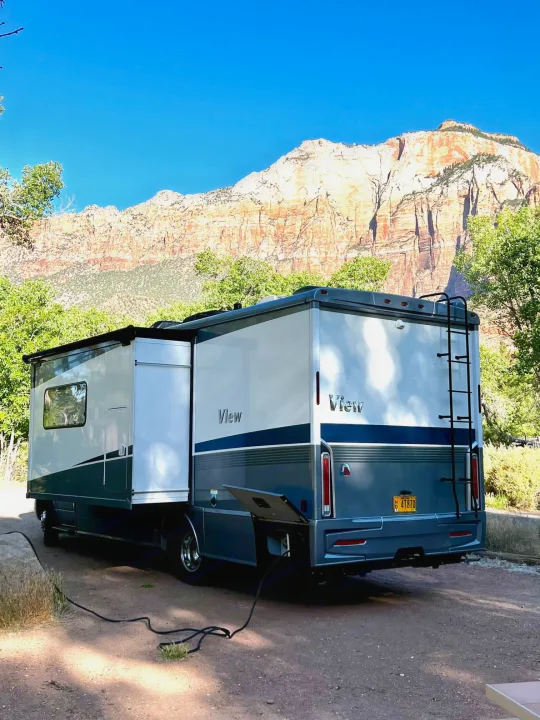 RV rental parked at a scenic campsite, with a modern motorhome against majestic mountains and green foliage.. Winnebago View 2022