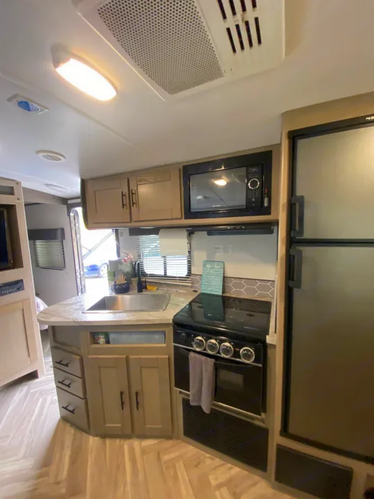 Well-equipped RV rental kitchen features sink, microwave, stove, fridge, and ample storage for comfortable mobile living.. Cruiser RV Shadow Cruiser 2021