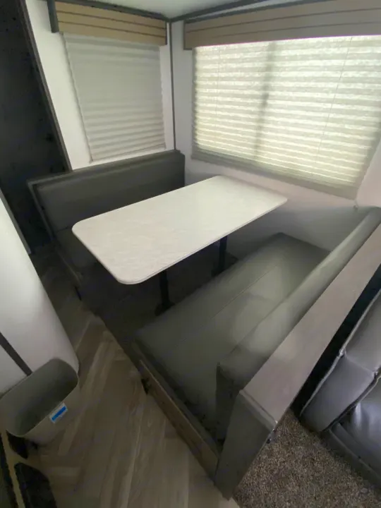 RV rental dinette: A white table with dark cushioned booth seating. Windows above have light-colored blinds.. Cruiser RV Shadow Cruiser 2021