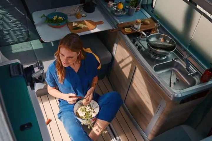 Woman enjoying a meal in a cozy rv rental with a modern kitchen and dining area.. Volkswagen California Coast T6.1 DSG7 2023