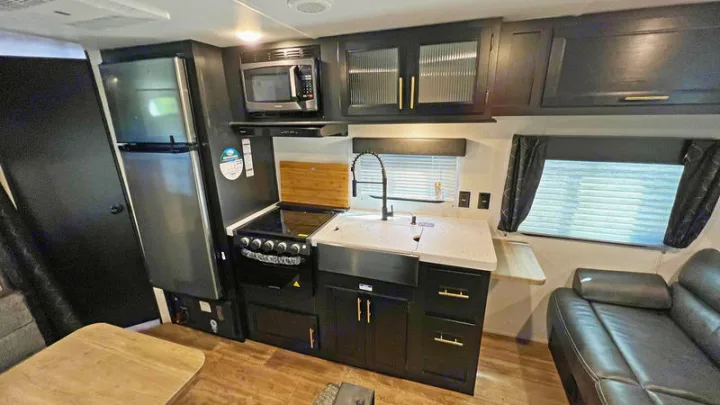 RV rental kitchen and living area with modern black cabinets, stainless appliances, and sofa.. Forest River Cherokee Grey Wolf Special Edition 2022