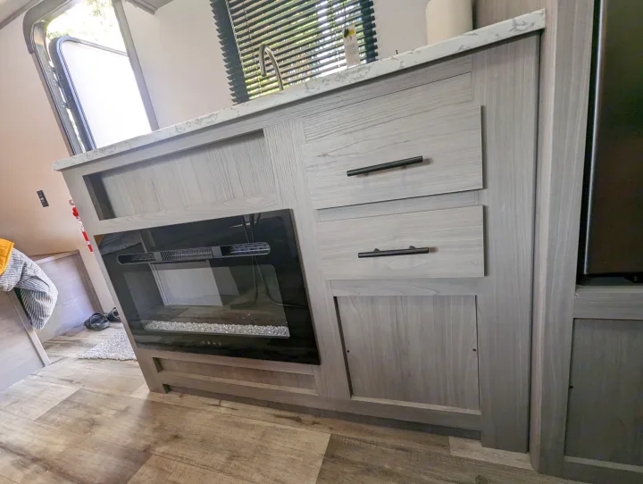 This modern RV rental features a well-equipped kitchen counter, electric fireplace, and ample wood-grain cabinetry.. Dutchmen Coleman Lantern 17B 2024