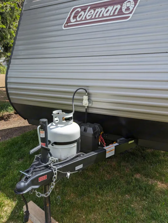 Front of a Coleman travel trailer (RV rental) with propane tanks, battery, and hitch assembly on grass.. Dutchmen Coleman Lantern 17B 2024