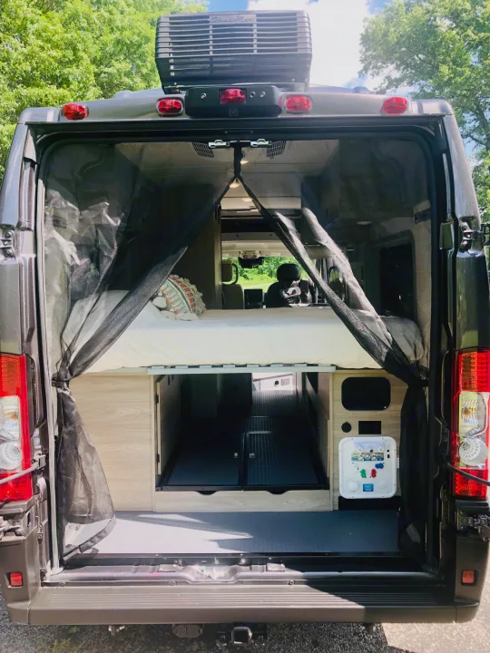 Open rear of a functional rv rental camper van, revealing a raised bed, spacious storage, and essential utility connections.. Winnebago Solis 2023