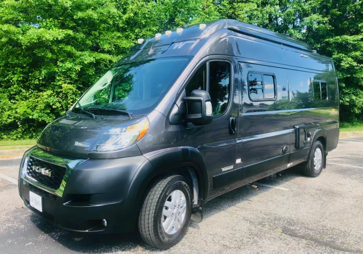 Gray Winnebago camper van for rv rental, parked outdoors with green trees in the background.. Winnebago Solis 2023
