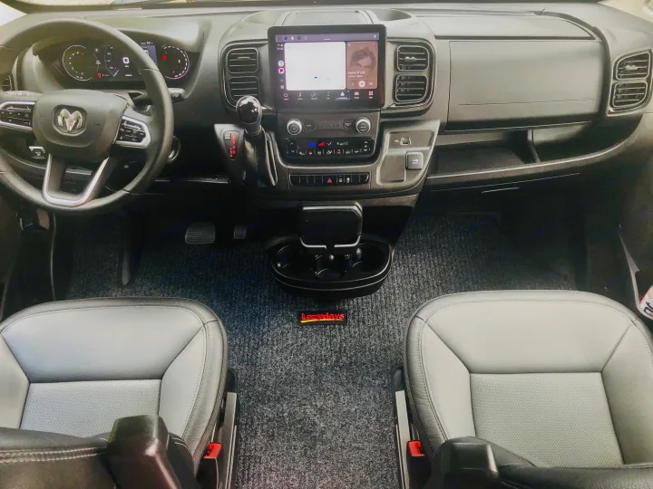 A clean Ram ProMaster RV rental interior: dashboard, steering wheel, large touchscreen, and front seats with "Lazydays" mat.. Winnebago Solis 2023