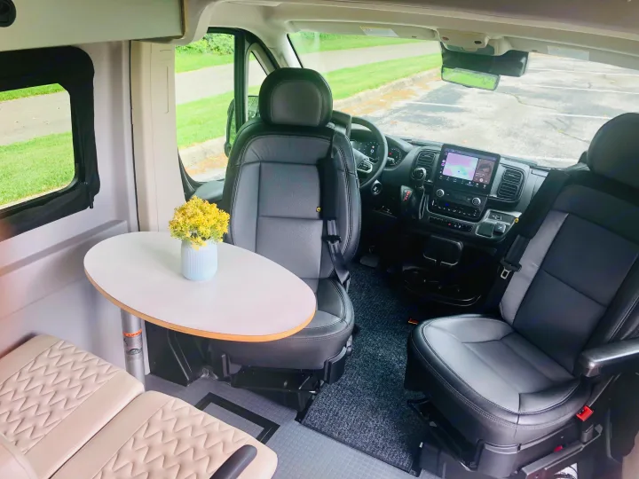Spacious RV rental interior with swiveling front seats, a dining table, and modern dashboard. Ideal for comfortable travel.. Winnebago Solis 2023