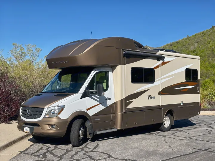 This two-tone Winnebago View RV rental, featuring brown and white, is parked on asphalt with a clear blue sky background.. Winnebago View 2017