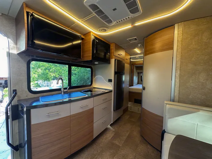 Bright, modern RV rental interior with a full galley, TV, and rear bedroom. Ambient lighting & wood accents create comfort.. Winnebago View 2017