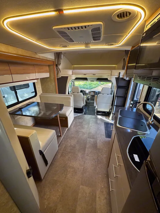 Spacious RV rental interior with bright lighting, featuring a kitchen area, dining booth, and an overhead bunk.. Winnebago View 2017