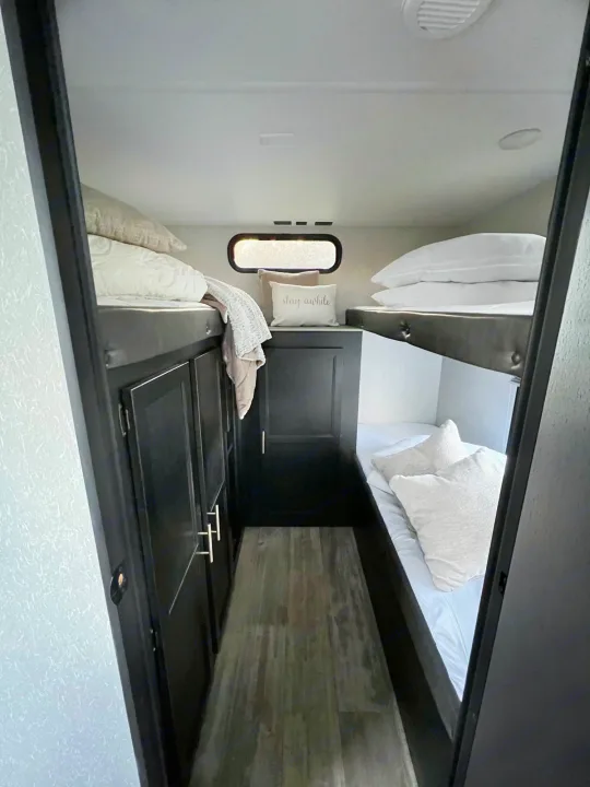 Cozy RV rental bunk beds with white linens, integrated dark storage, and a small window for a comfortable stay.. Forest River Cherokee Grey Wolf 2021
