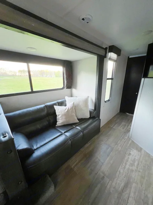 Step inside this RV rental, featuring a spacious living area with a comfortable black sofa and a scenic window view.. Forest River Cherokee Grey Wolf 2021