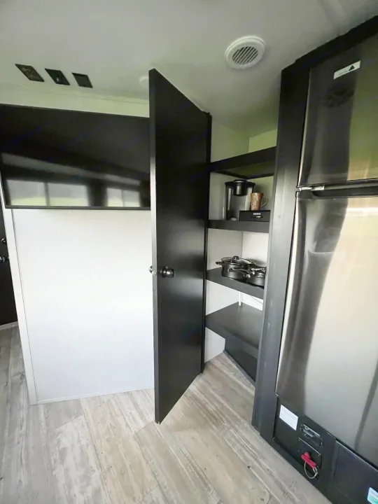 RV rental interior showing a kitchen pantry with Keurig and pots, a large TV, and stainless steel fridge.. Forest River Cherokee Grey Wolf 2021