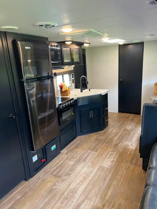 Modern RV rental interior with a spacious kitchen, black appliances, light wood-look flooring, and dark cabinets.. Forest River Cherokee Grey Wolf 2021