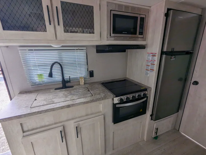 Explore this practical RV rental kitchen showcasing a sink, stove, microwave, and refrigerator for your travels.. Grand River Comfortline 20bh 2022