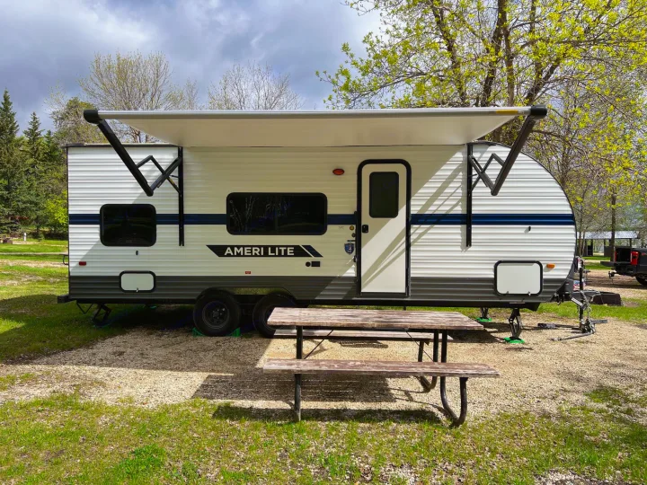 Spacious Ameri Lite RV rental parked at a scenic campsite with an extended awning and picnic table. Ideal for outdoor travel.. Gulf Stream Ameri-Lite 2022