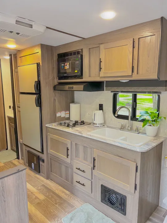Clean RV rental kitchen: fridge, microwave, stove, sink, light wood cabinets. Ideal for travel adventures.. Gulf Stream Ameri-Lite 2022
