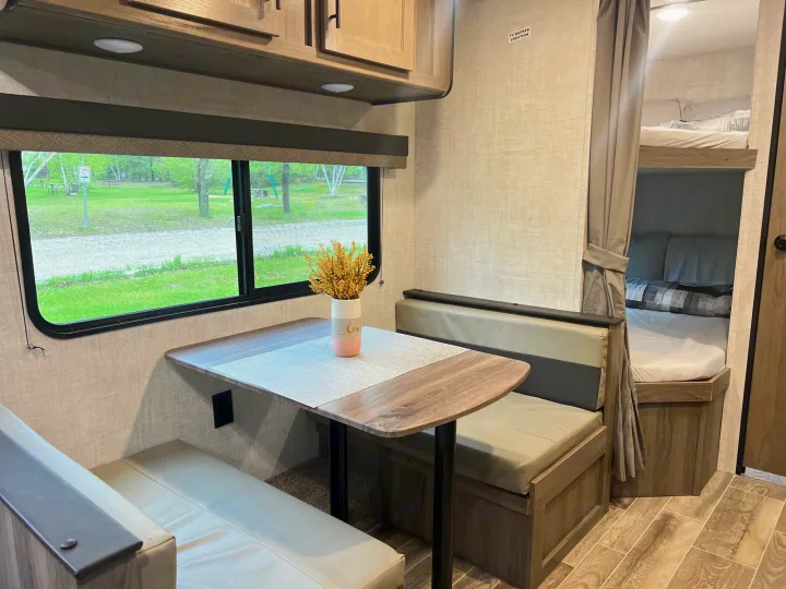 This RV rental showcases a cozy dinette with a window overlooking green space and integrated bunk beds.. Gulf Stream Ameri-Lite 2022